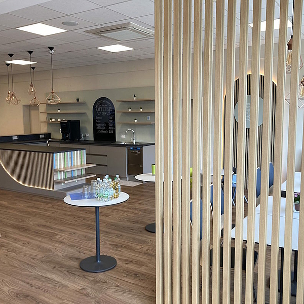 Großzügige Sondertheke mit indirekter LED-Beleuchtung, Akustikpaneelen und Holzraumteiler in einem hellen, modern gestalteten Gemeinderaum.