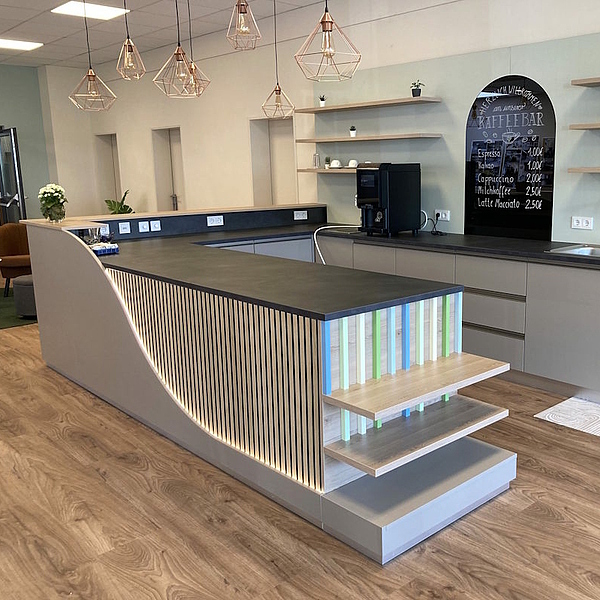 Moderner Thekenbereich mit geschwungener Front, vertikalen Holzleisten, integrierter Beleuchtung und offenen Regalböden im Hintergrund.